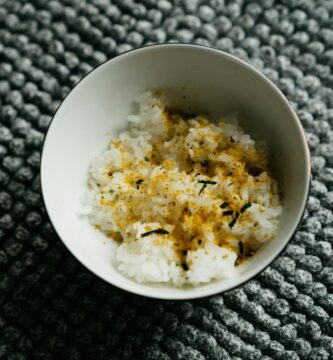 Close-up of Japanese rice bowl topped with furikake, a traditional seasoning, on a textured surface.